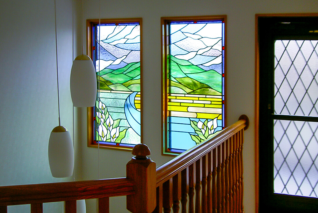 階段吹き抜け部分に取り付けたカラー（花）と風景をモチーフにデザインした2連のステンドグラス作品